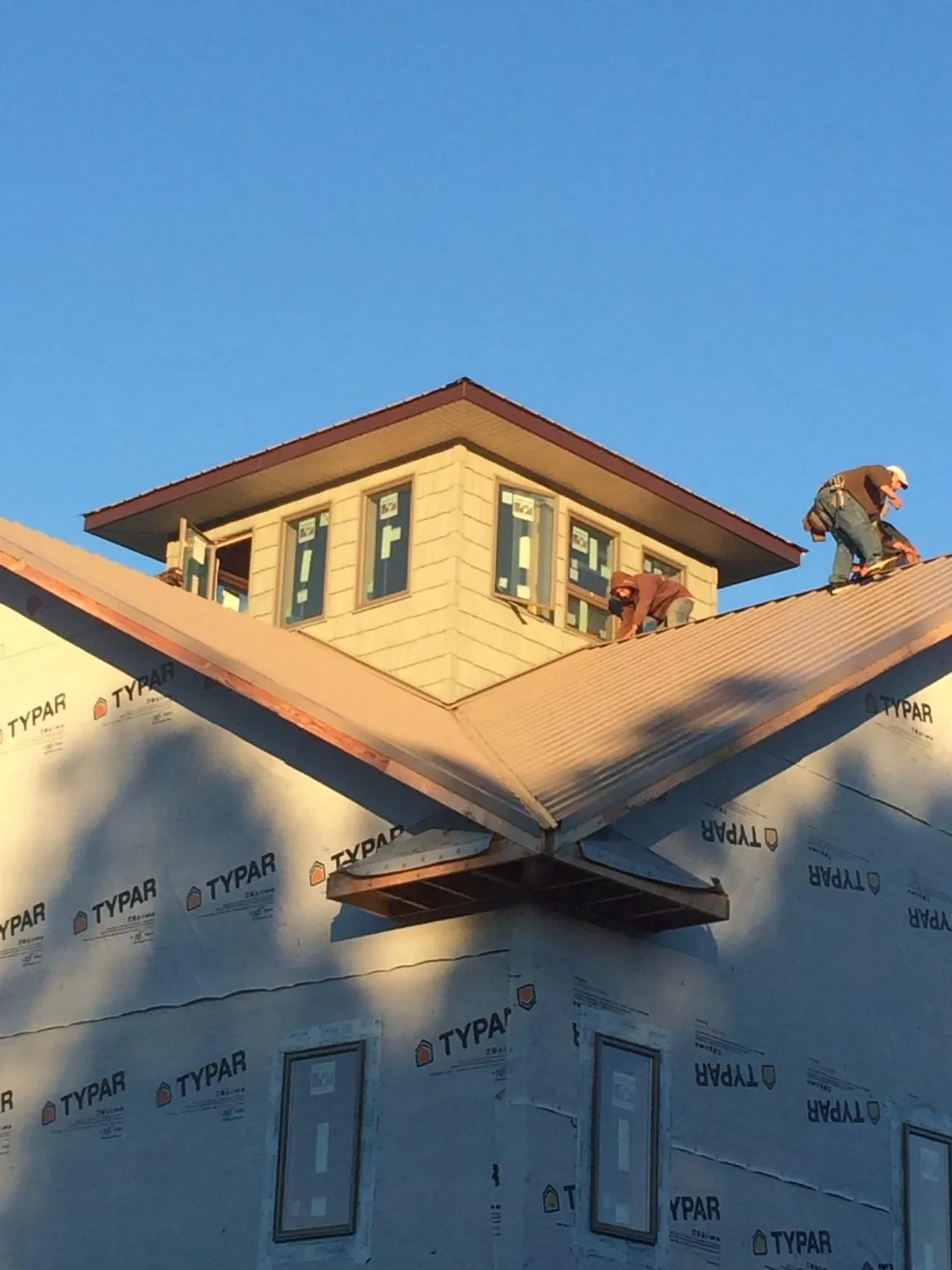 Roofers working around a rooftop cupola on a new metal roof at sunset — Roof Waterproofing in Lakewood by Roofing Brothers